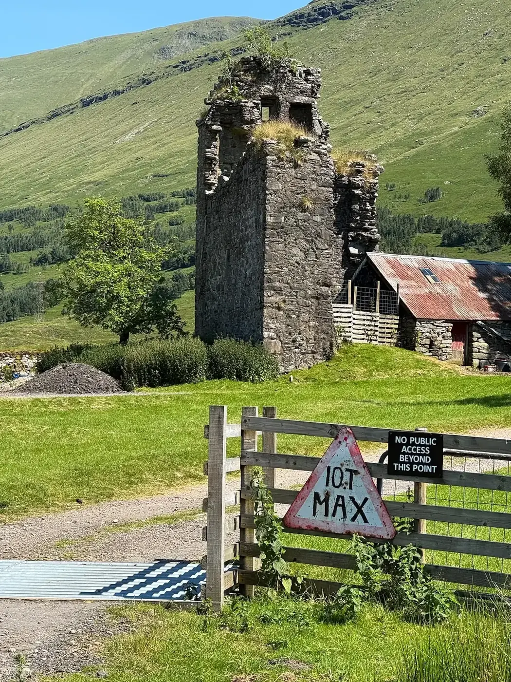 Achallader Castle tower beside a farm building and fenced entrance