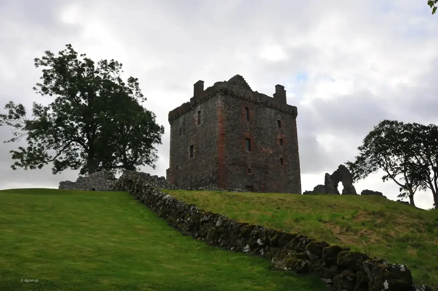 Balvaird Castle tower above a grass slope and stone wall