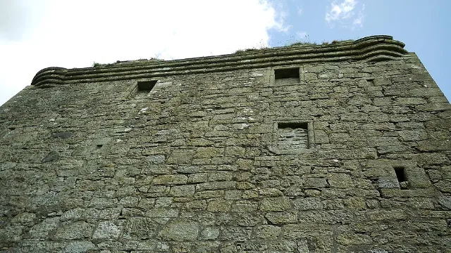 Upward view of Barr Castle's stone wall, blocked openings and moulded parapet.