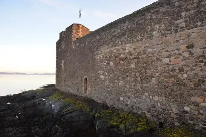 Sunlit outer wall of Blackness Castle above the rocky shore