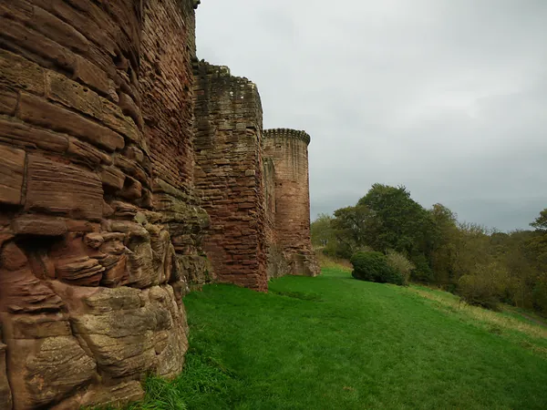 Bothwell Castle outer walls beside a grassy slope and trees