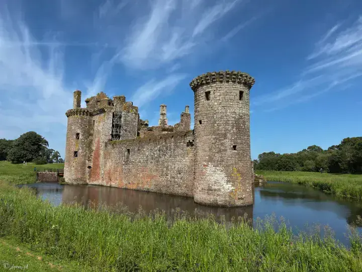 Round corner tower and long curtain wall beside Caerlaverock Castle's moat