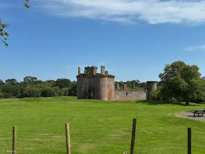 Caerlaverock Castle across a broad lawn beside trees