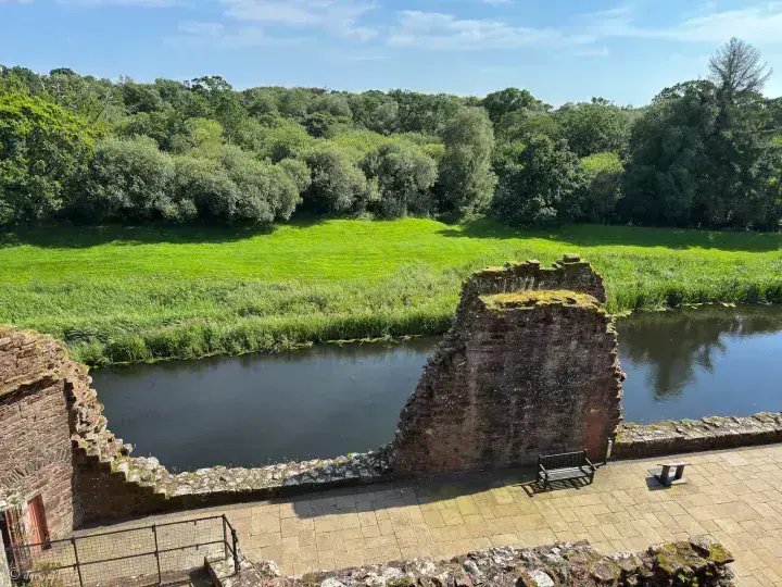 View across Caerlaverock Castle's ruined wall to the moat and woodland