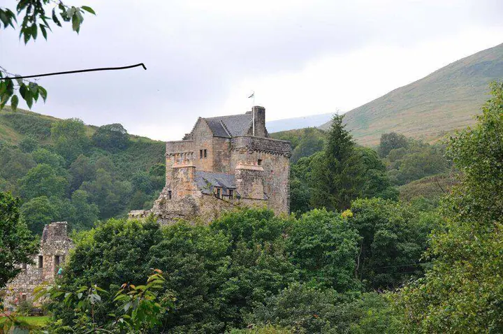 Castle Campbell rising above woodland with a hillside beyond