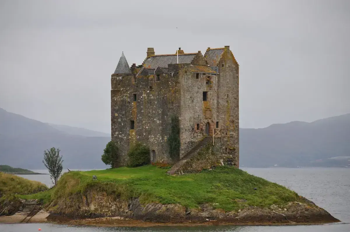 Castle Stalker’s stone tower on a grassy island, with mountains behind