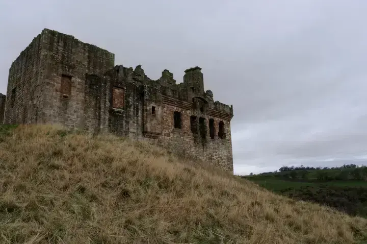 Long ruined wall of Crichton Castle above dry grass