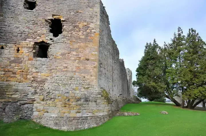 Rounded corner of Dirleton Castle's thick stone wall beside the lawn
