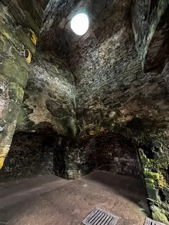 Dark stone chamber lit through a high round opening at Dirleton Castle
