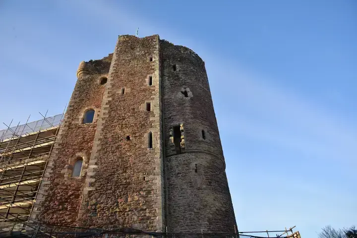 Doune Castle's tall tower beside scaffolding under blue skies