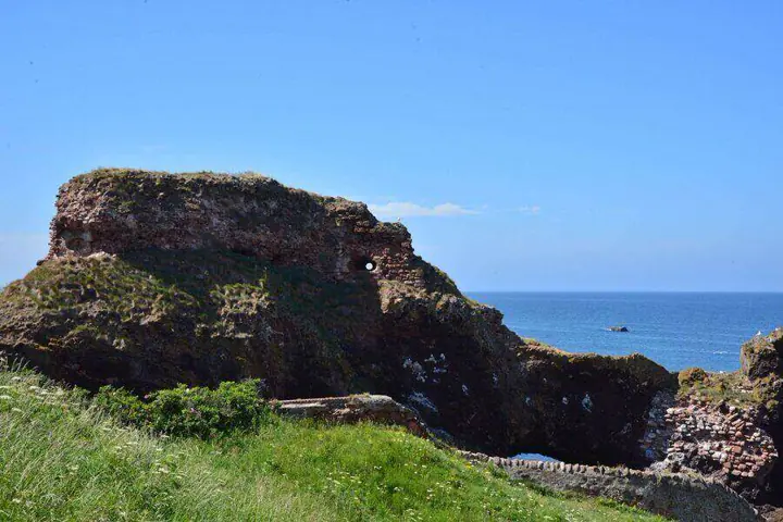Grassy foreground and low Dunbar Castle ruins overlooking the sea