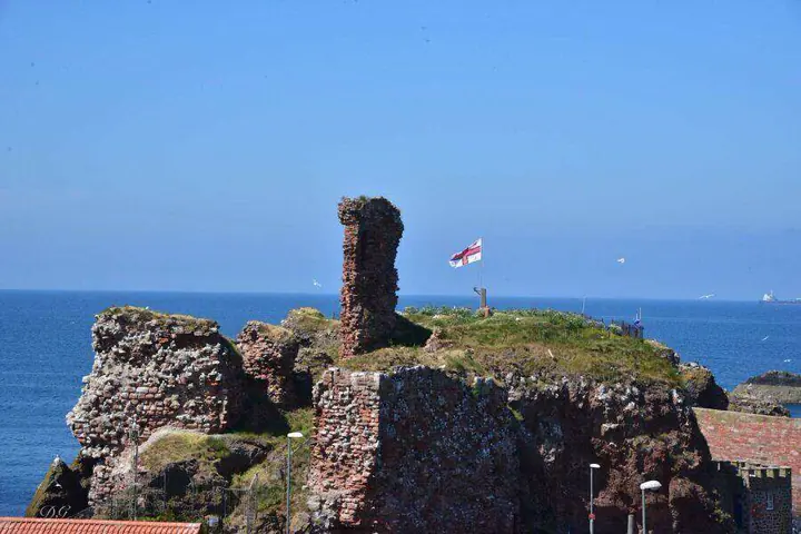 Dunbar Castle ruins with a flag and harbour rooftops beside the sea