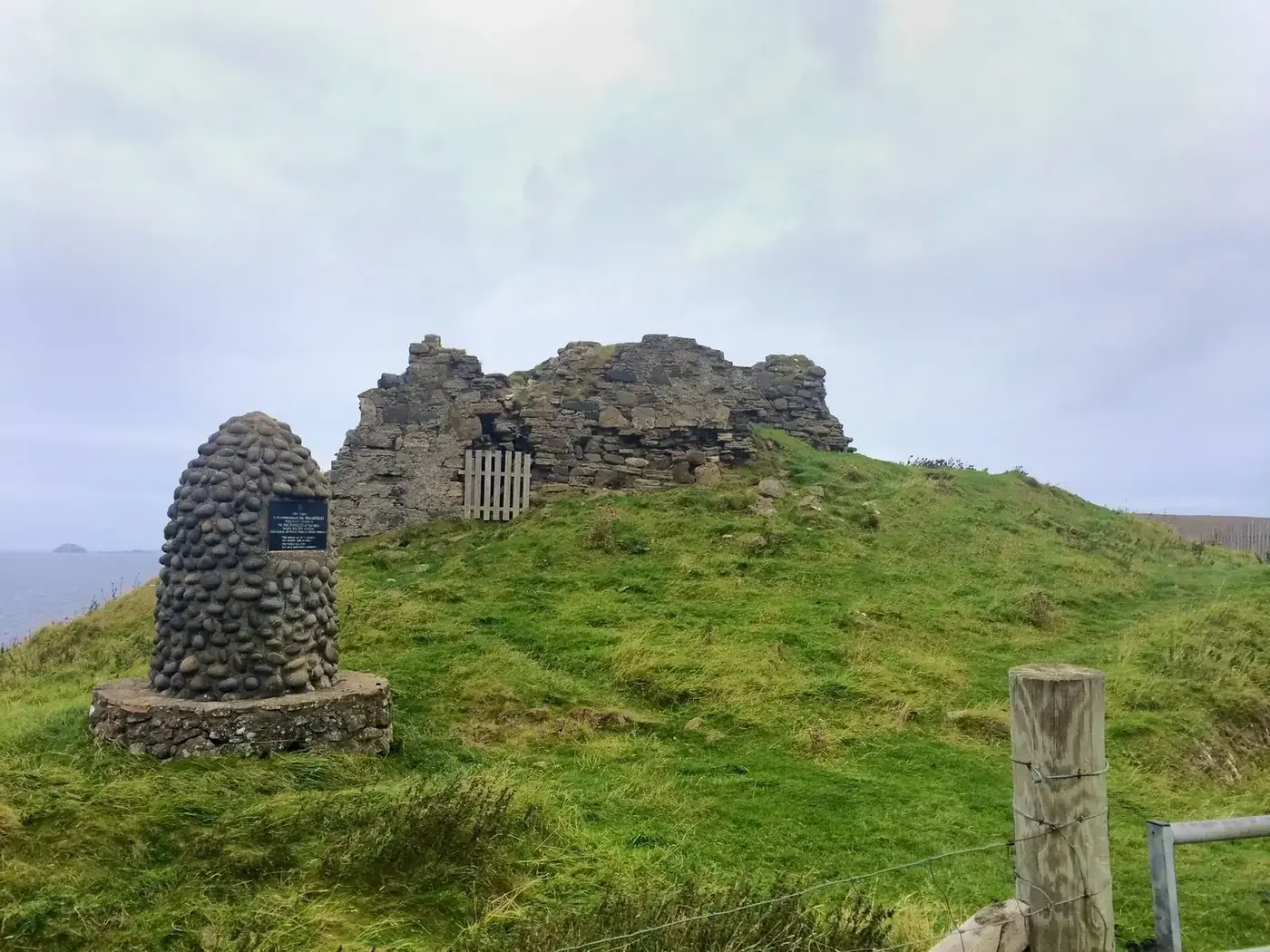 Duntulm Castle ruins on a grassy mound beside a stone memorial