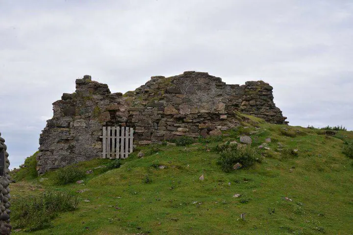 Duntulm Castle wall remnants and fenced opening on the grassy slope