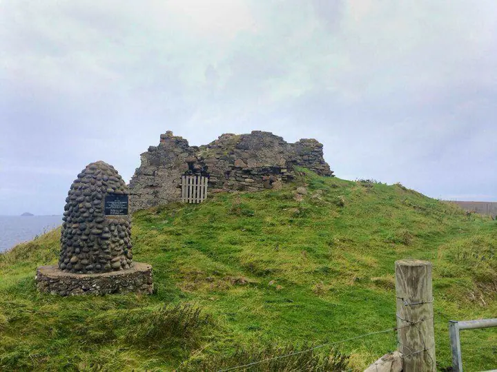 Duntulm Castle ruins on a grassy mound beside a stone memorial
