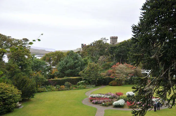 Garden lawn and flower beds with Dunvegan Castle partly hidden by trees
