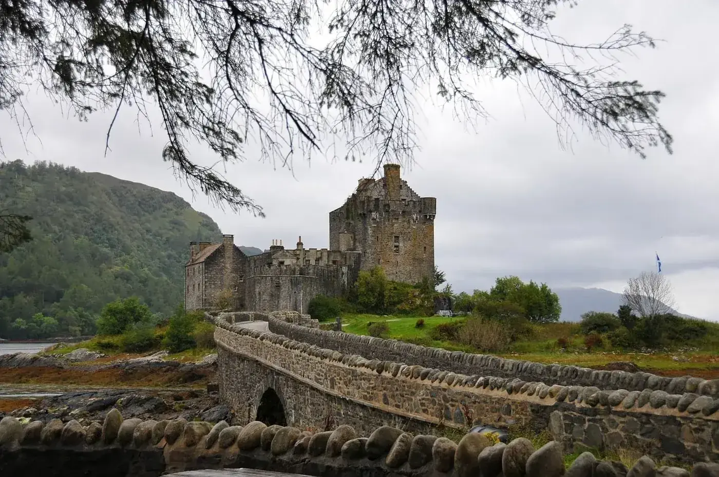 Eilean Donan Castle and its arched stone bridge beneath overhanging branches