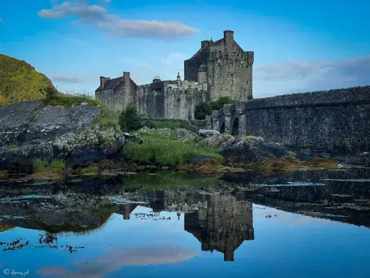 Eilean Donan Castle tower and stone bridge mirrored in the water below