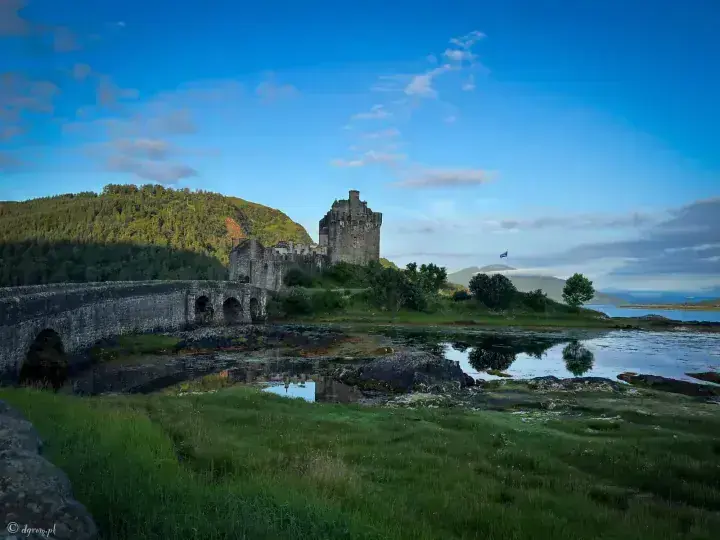 Eilean Donan Castle and arched bridge above tidal pools and green shoreline grass