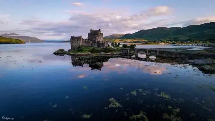 Wide evening view of Eilean Donan Castle and its bridge reflected in the loch