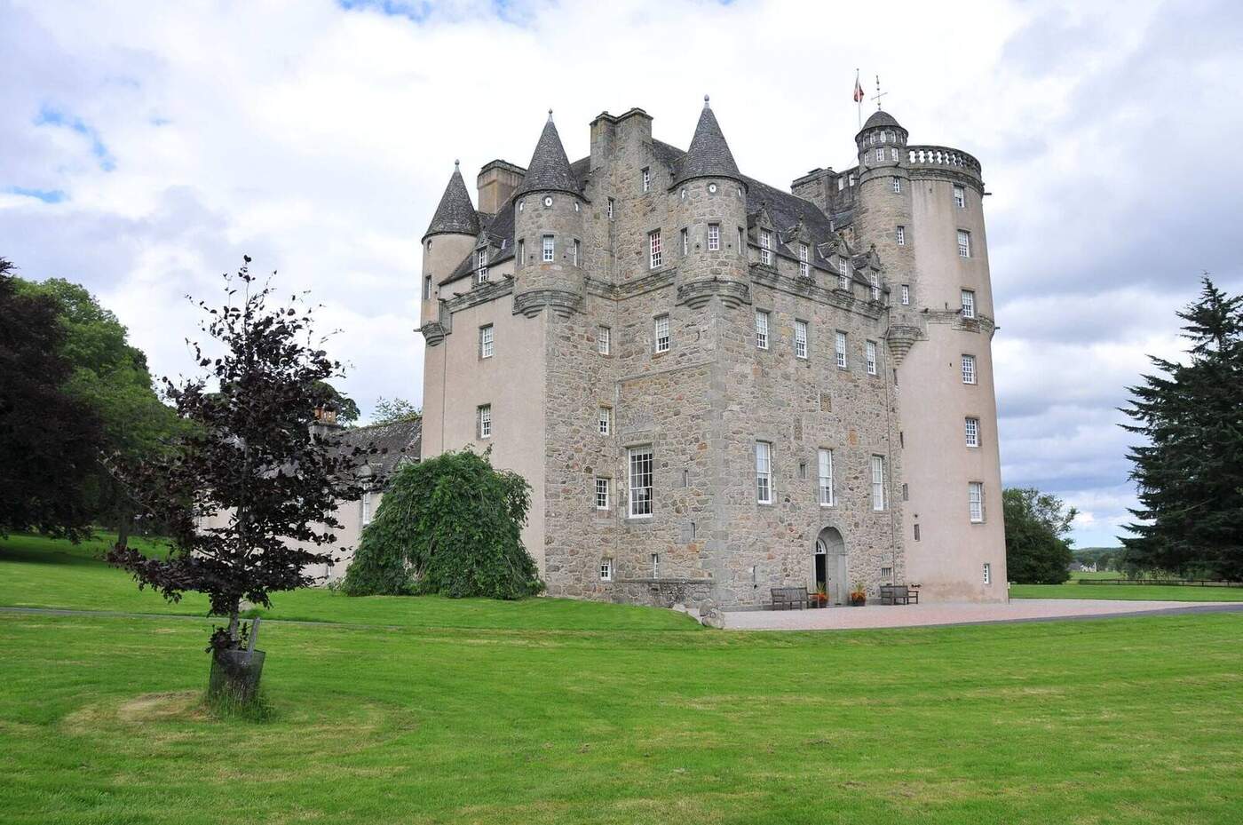 Castle Fraser with pale walls and pointed turrets beside a lawn