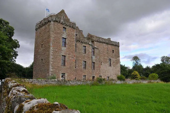 Huntingtower Castle viewed beyond a low stone wall and green grass
