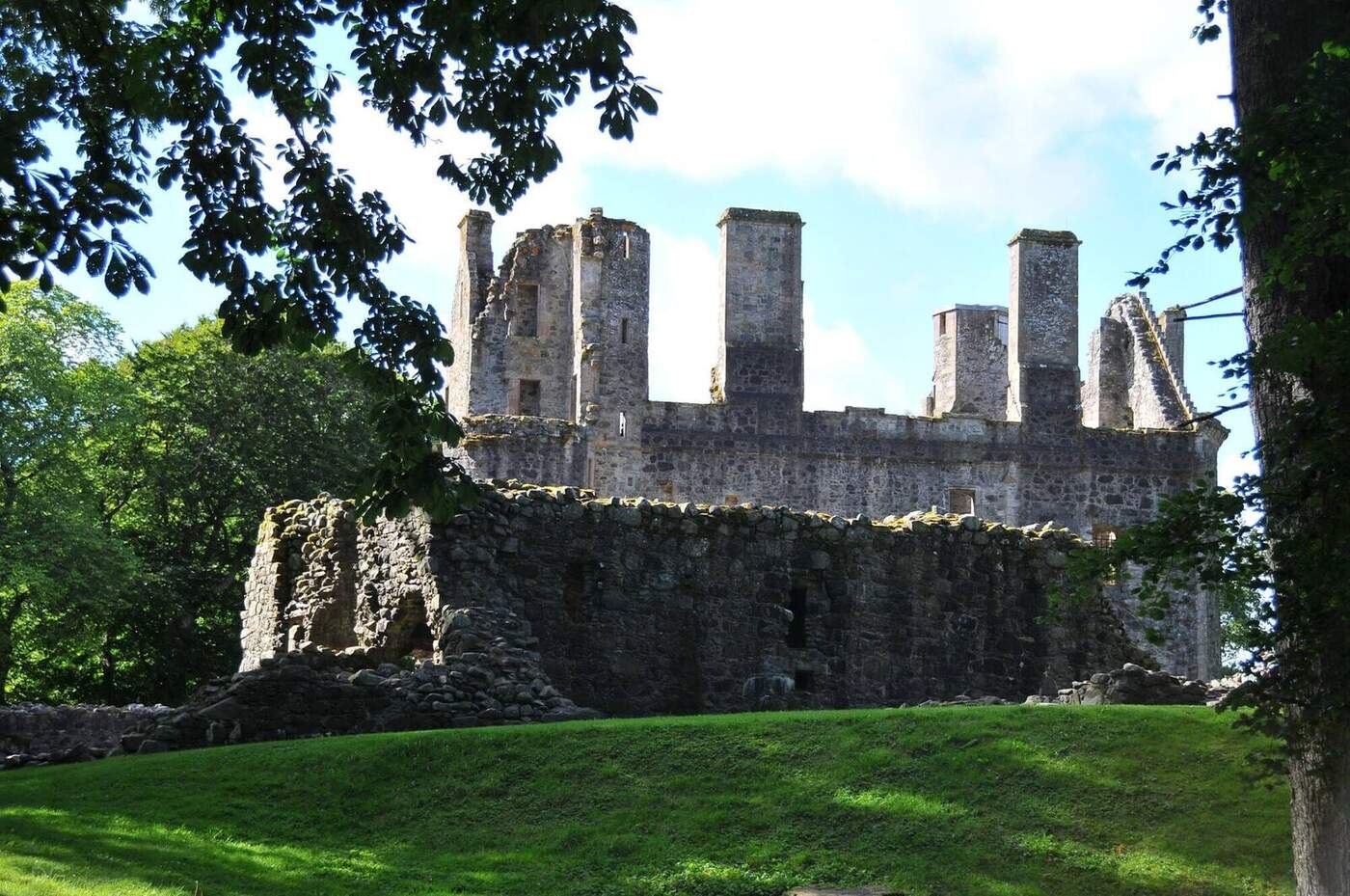 Roofless Huntly Castle walls and chimneys framed by leafy branches