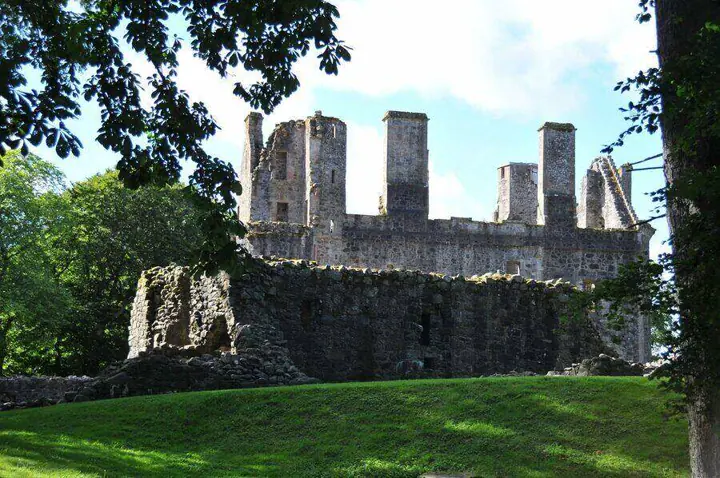 Roofless Huntly Castle walls and chimneys framed by leafy branches