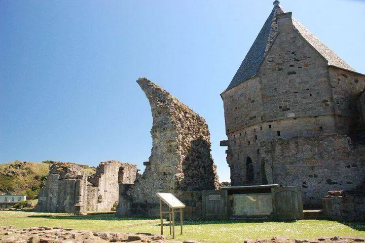 Tall ruined wall beside Inchcolm Abbey's pointed-roof building