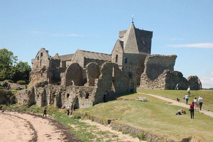 Visitors walking beside Inchcolm Abbey's roofless walls above the beach