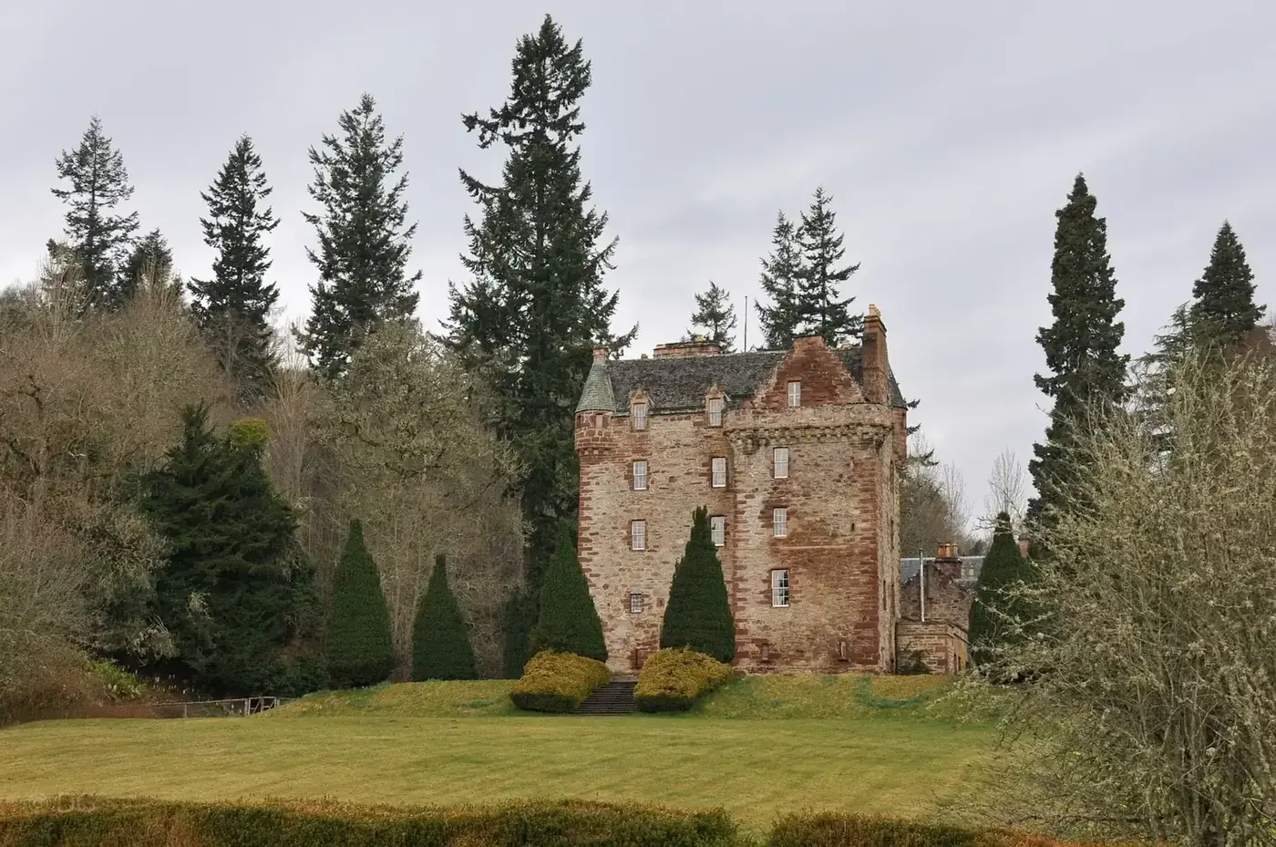 Castle Leod framed by tall trees and clipped conifers