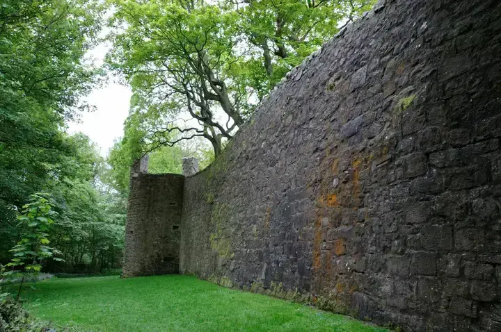 Long stone wall of Loch Leven Castle beside grass and trees