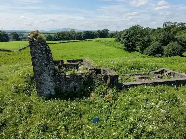 Lochwood Castle ruins across a meadow with trees and farmland behind