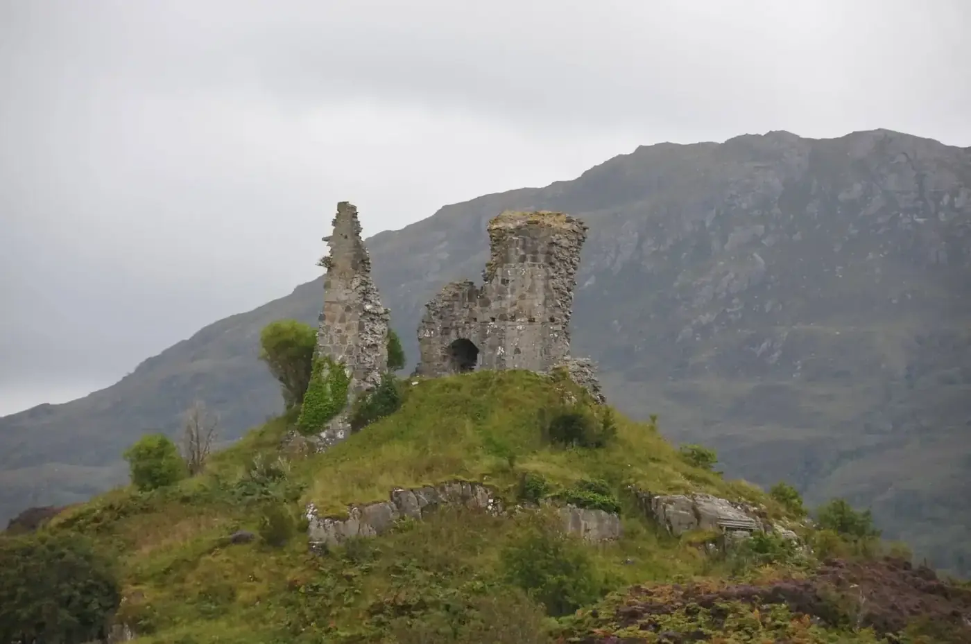 Maol Castle ruins on a rocky hill with mountains behind