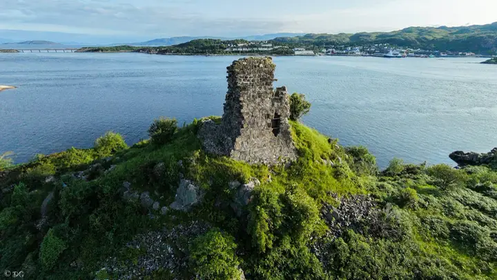 Maol Castle wall on a green promontory with blue water beyond