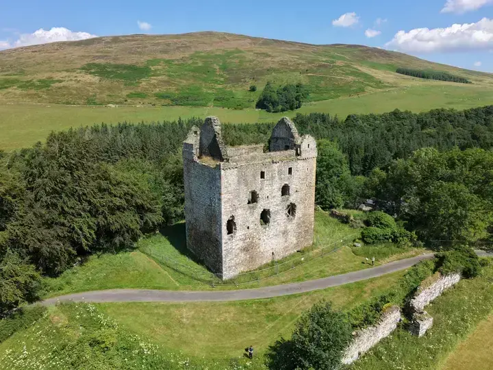 Newark Castle among trees beneath a grassy hill