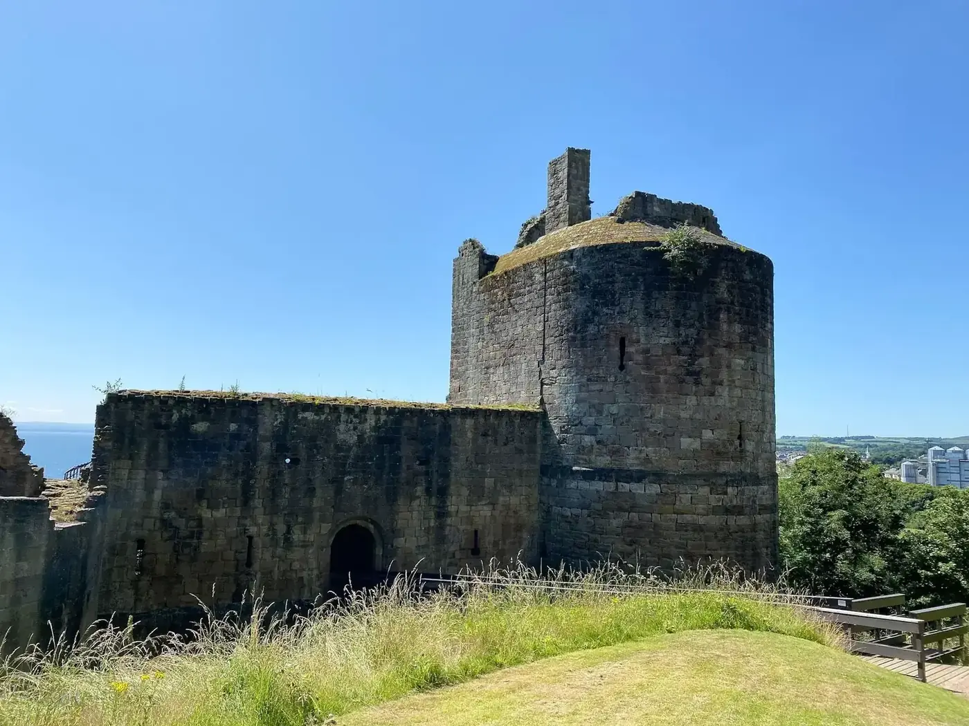 Ravenscraig Castle's rounded tower and entrance wall beside a grassy bank