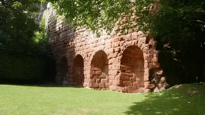 Sunlit arches in Roslin Castle's ruined wall beside a green lawn