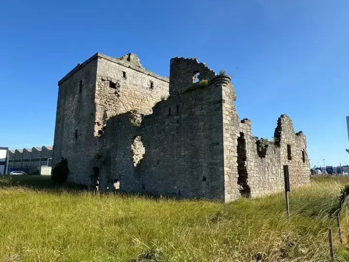 Rosyth Castle's square tower behind broken stone walls and tall grass