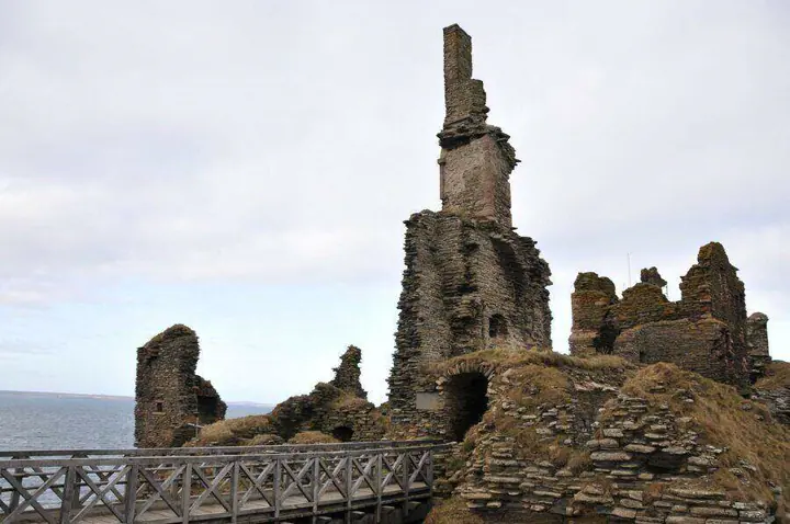 Wooden footbridge beneath a tall ruined chimney at Sinclair Girnigoe Castle