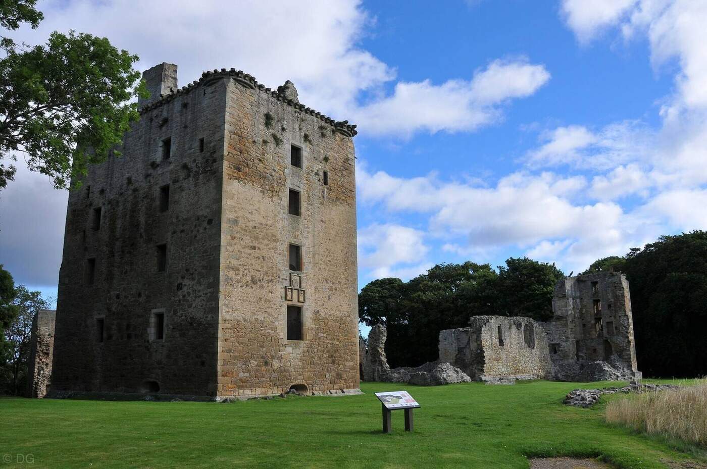 Tall stone tower of Spynie Palace beside lower ruins and a lawn