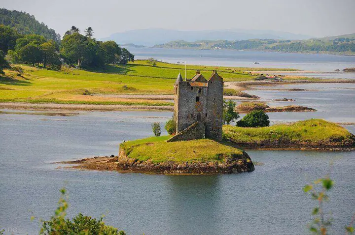 Castle Stalker across blue water with coastal fields and distant hills
