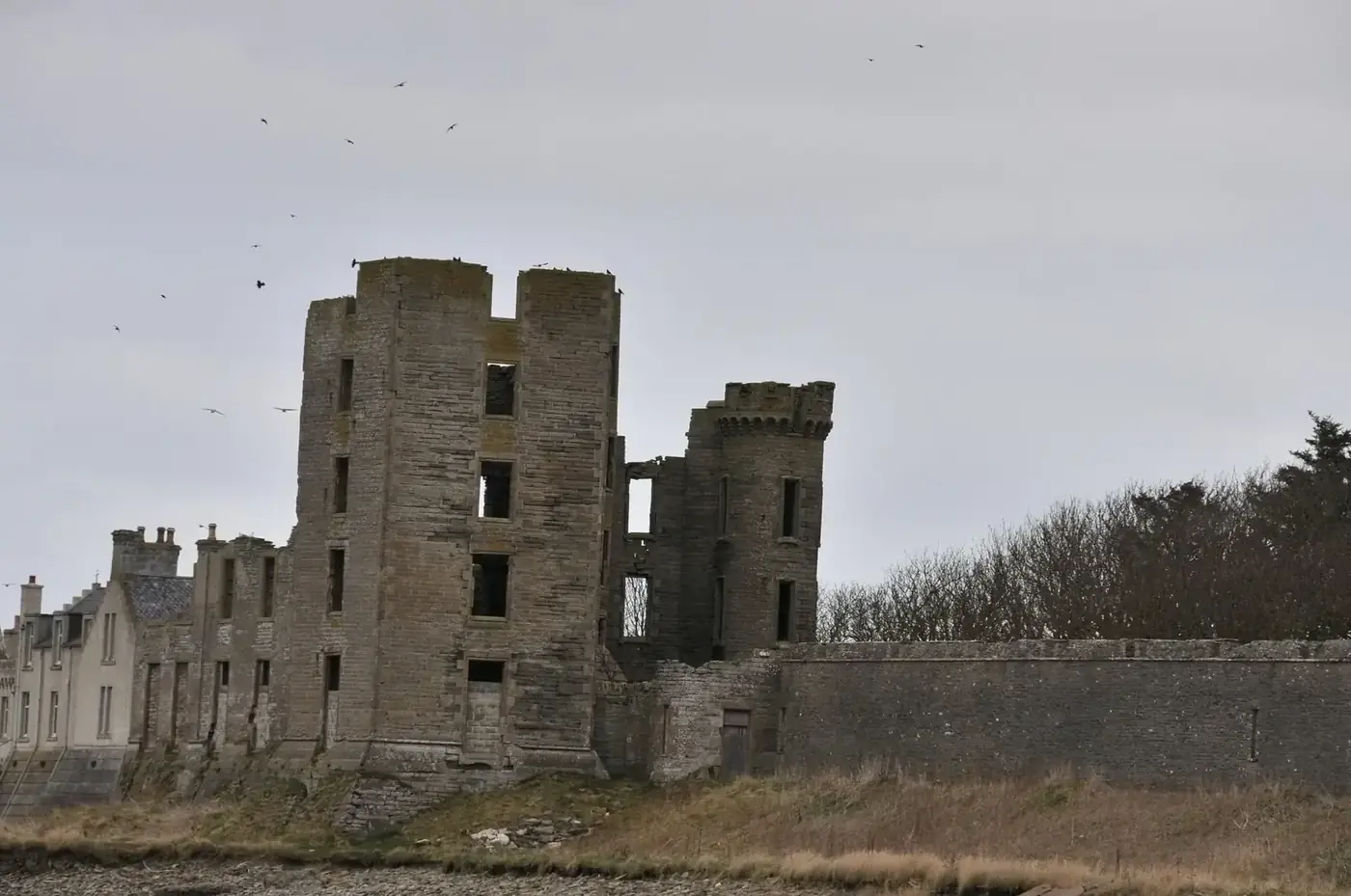 Roofless towers of Thurso Castle beside a long stone wall