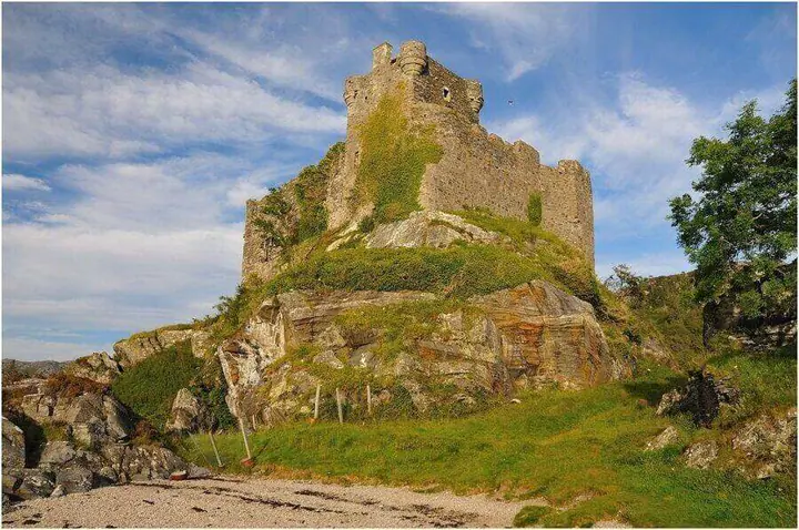 Tioram Castle ruins on a rocky mound beside a sandy shoreline