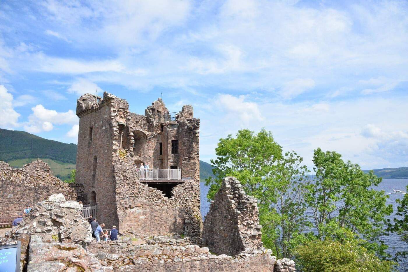 Ruined tower of Urquhart Castle beside leafy trees and water